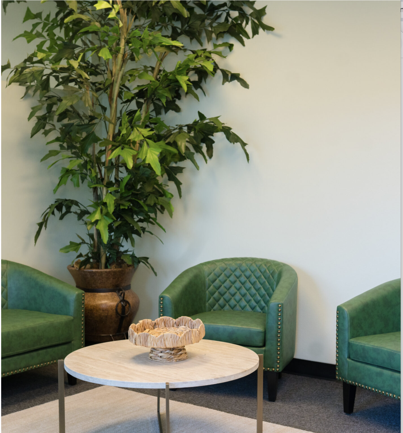 Suite Care lounge with sage green tufted chairs and a tall indoor tree